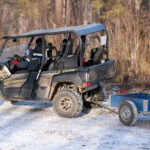 Plne naložená pracovná štvorkolka s pripojeným vozíkom prevážajúca ťažký náklad v teréne.